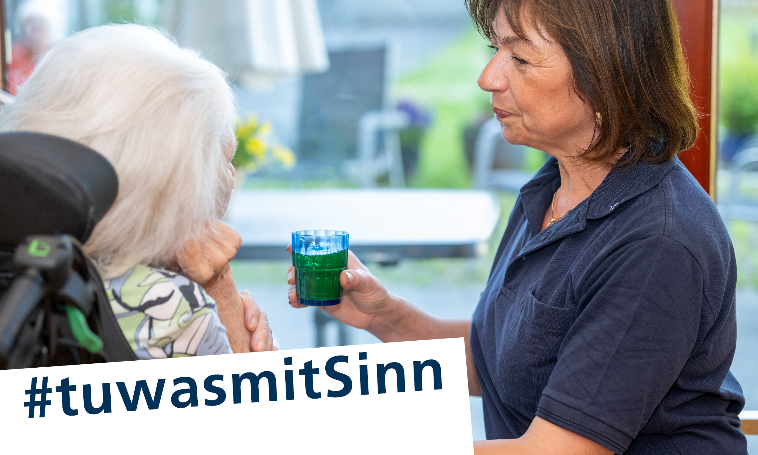 Eine Pflegekraft gibt einer Bewohnerin ein Glas Wasser